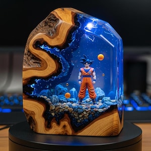 May include: A unique resin art piece featuring a Dragon Ball Z character within a blue and clear resin block. The wooden base and sides contrast with the vibrant blue interior, which includes a character figurine and orange spheres. The piece is displayed on a black rotating stand.