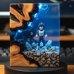 May include: A resin art piece featuring a Dragon Ball Z character, Vegeta, standing on a rocky platform. The background depicts a blue, stormy scene with lightning. The piece is encased in a rectangular block with wood grain on one side.