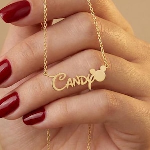 Pu&ograve; includere: Una collana color oro con il nome "Candy" in corsivo. Un piccolo design a forma di testa di Mickey Mouse &egrave; accanto al nome. La collana &egrave; tenuta da una mano con lo smalto rosso.