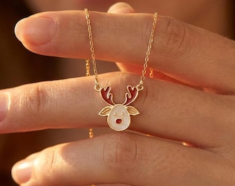Op de afbeelding: Een goudkleurige ketting met een rendierhanger. De hanger heeft een wit gezicht, rode geweien en een gouden omtrek. De ketting wordt door een hand omhoog gehouden.