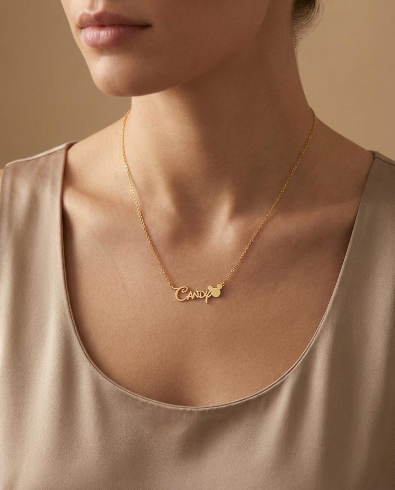 May include: A gold-colored necklace with the name "Candy" in a cursive font. A small mouse-shaped design is next to the name. The necklace is worn around the neck.