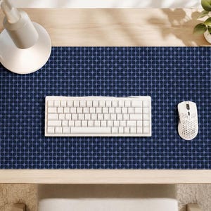 May include: A rectangular desk mat featuring a dark blue and light blue geometric pattern of repeating four-pointed stars. The mat is positioned on a wooden surface with a white mechanical keyboard and a white computer mouse placed on top.