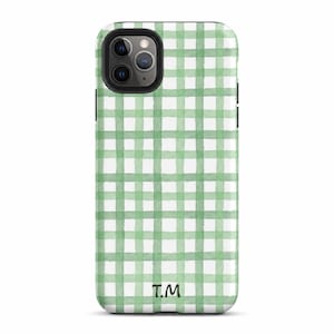 Puede incluir: Una funda para smartphone con un patrón de cuadros vichy en verde claro y blanco estilo acuarela. El diseño incluye un recorte negro para la lente de la cámara en la parte superior izquierda y las letras mayúsculas negras T.M en la parte inferior.