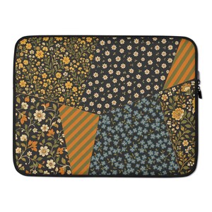 Puede incluir: Una funda rectangular para portátil con un diseño de patchwork de varios patrones florales en tonos amarillo mostaza, crema, verde oliva y azul pizarra, intercalados con secciones de rayas diagonales naranjas y verde oliva.