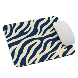 Peut inclure: Un tapis de souris rectangulaire arborant un motif de rayures zébrées bleu marine foncé et crème. Une souris d'ordinateur blanche et lisse est placée sur le côté droit du tapis de souris, reposant sur la surface à motifs de cet accessoire.