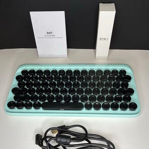 May include: A mint green mechanical keyboard with black round keys. The keyboard has a retro design and includes a USB cable, a box labeled "DOT", and another white box. The keyboard is designed for use with a computer.