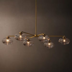 May include: A modern chandelier with six clear glass globe shades. The fixture has a brass finish and is suspended from a central rod. Each globe houses a single light bulb, creating a warm, inviting glow. The design is sleek and contemporary.