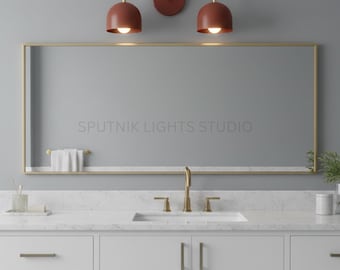 May include: A modern bathroom vanity set featuring a large rectangular mirror with a gold frame. Above the mirror are two terracotta-colored dome-shaped lights. The vanity has a white countertop, a white sink, and white cabinets with gold hardware. The text "SPUTNIK LIGHTS STUDIO" is visible on the mirror.