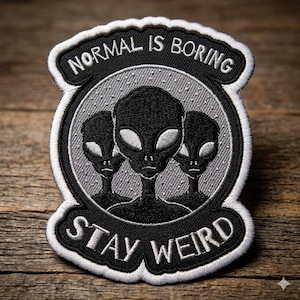 May include: Embroidered patch featuring three black alien figures with large eyes, set against a gray speckled background. The patch has the text "NORMAL IS BORING" above the aliens and "STAY WEIRD" below, all in white lettering on a black background.