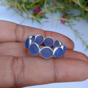 Può includere: Un anello caratterizzato da una serie di pezzi circolari di vetro marino blu traslucido incastonati in una fascia di metallo color argento. Gli elementi circolari in vetro sono disposti fianco a fianco per formare la circonferenza dell'anello.