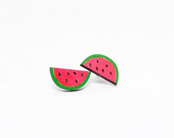 Könnte beinhalten: Zwei Ohrringe in Form von Wassermelonenscheiben. Jeder Ohrring hat ein rotes Innenteil mit schwarzen Samendetails, eine grüne Schale und eine schwarze Kontur, vor weißem Hintergrund.