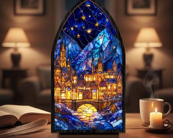 Può includere: Una lampada in vetro colorato raffigurante un paesaggio urbano notturno con un ponte, edifici e montagne. La lampada ha una cornice in legno scuro ed è illuminata da luci calde gialle e arancioni. Lo sfondo presenta un cielo stellato.