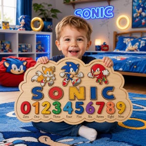 May include: A wooden puzzle board featuring the characters Tails, Sonic, and Knuckles at the top. Below the characters, the word SONIC is printed in large letters, followed by the numbers 0 through 9, each with its corresponding word name.