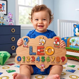May include: A wooden puzzle board shaped like a cloud featuring the name LEO in large colourful letters, with the numbers zero through nine printed below, accompanied by small character cutouts of Sonic, Tails, Knuckles, and Amy Rose.