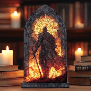 Puede incluir: Lámpara de estilo vidriera que representa a un caballero con una espada, sobre un fondo de fuego. La lámpara tiene un marco gris oscuro y un interior cálido y brillante. El caballero está con armadura completa, con una capa fluida.