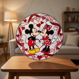Op de afbeelding: Een rond gebrandschilderd glazen raam met Mickey en Minnie Mouse. Het ontwerp bevat rode harten en linten op een witte achtergrond. Het raam wordt opgehangen door een zilveren ketting. De diameter is ongeveer 25 cm.