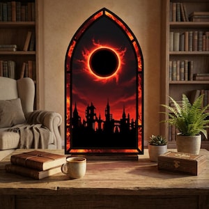 May include: A gothic-style illuminated panel featuring a fiery red and black eclipse design. The silhouette of a city skyline is visible below the eclipse. The panel is set on a wooden table with books and a coffee cup.