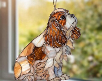 Puede incluir: Adorno de perro de vidriera en tonos marrón, crema y blanco. El perro está representado en posición sentada, con detalles precisos y una textura particular. El adorno está diseñado para colgarse y captar la luz.