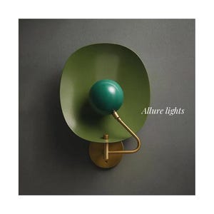 Könnte beinhalten: Moderne Wandleuchte mit grünem, ovalem Schirm und grüner Kugel. Der Arm und die Basis sind messingfarben. Der Text "Allure lights" ist auf der rechten Seite zu sehen.