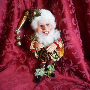 May include: A whimsical Christmas elf figurine with a white beard and a red and gold costume. The elf is holding a small golden bell and has a mischievous grin.