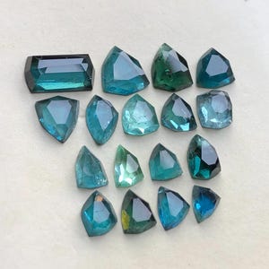 Peut inclure: Une collection de dix-sept pierres précieuses facettées en vrac dans diverses nuances de bleu sarcelle, de bleu et de vert. Les pierres présentent des formes géométriques variées, dont une pièce rectangulaire et plusieurs coupes irrégulières, angulaires et en forme de bouclier.