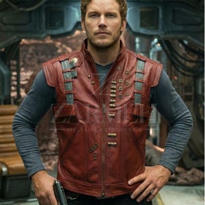 Puede incluir: Un chaleco de cuero rojo con detalles plateados y elementos decorativos. El chaleco tiene cierre de cremallera y varios bolsillos. El texto "FEELS LIKE A SECOND SKIN" es visible. El chaleco se lleva sobre una camiseta gris de manga larga.