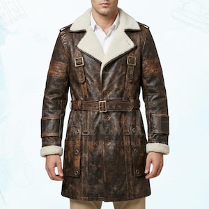 May include: A brown leather coat with a cream-colored shearling collar and cuffs. The coat features a belted waist, multiple buckles, and decorative stitching on the shoulders. The coat is approximately 48 inches long.