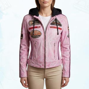 Peut inclure: Veste en cuir rose pâle avec capuche noire et fermeture éclair. La veste comporte plusieurs écussons avec du texte et des motifs de course. Des rayures violettes verticales ornent les manches. La veste est portée avec un haut blanc et un pantalon beige.