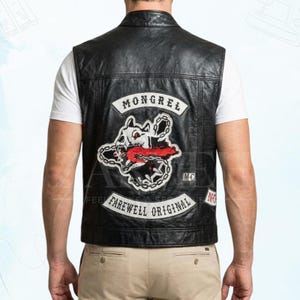 Puede incluir: Chaleco de cuero negro con un parche "Mongrel Farewell Original" que presenta un gráfico de calavera de perro gruñendo con detalles en rojo. El chaleco tiene un estilo motero clásico con cuello y costuras visibles.