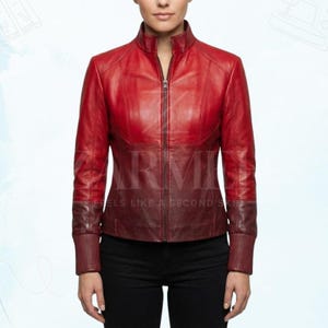 Pode incluir: Casaco de couro vermelho com gola alta e zíper completo. O casaco tem um gradiente de cor, passando de um vermelho mais claro no topo para um tom mais escuro na parte inferior. As mangas têm punhos canelados. O texto "FEELS LIKE A SECOND SKIN" é visível.