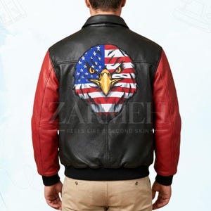 Könnte beinhalten: Schwarze Leder-Bomberjacke mit roten Ärmeln. Auf der Rückseite befindet sich eine große Grafik eines amerikanischen Flaggenadlers. Der Text "ZARMEH - FEELS LIKE A SECOND SKIN" ist auf die Jacke gedruckt.
