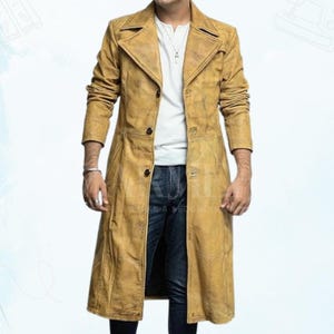 Könnte beinhalten: Ein langer, hellbrauner Ledermantel im klassischen Trenchcoat-Design. Der Mantel hat einen Reverskragen, Knopfverschlüsse und eine taillierte Passform. Er wird über einem weißen Hemd und blauen Jeans getragen.