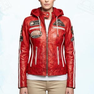 Könnte beinhalten: Rote Lederjacke mit Kapuze, weißen Streifen auf den Ärmeln und verschiedenen Aufnähern. Die Jacke hat einen Reißverschluss und zwei Vordertaschen. Aufnäher sind "Limited Edition" und "Speed Race Motorcycles".