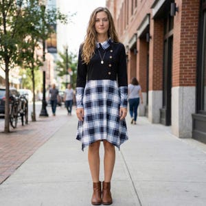 May include: A long-sleeved dress featuring a black bodice and a blue and white plaid skirt. The dress has a collared neckline and is accented with wooden buttons. The model is wearing brown ankle boots.