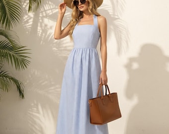 May include: A light blue and white pinstriped maxi dress with a square neckline and thick shoulder straps. The dress features a fitted bodice and a long, flowing skirt. A tan straw hat, dark sunglasses, and a brown leather tote bag are included.