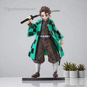 Könnte beinhalten: Figur eines Charakters aus der Anime-Serie Demon Slayer. Die Figur trägt eine braune Uniform mit einem grün-schwarz karierten Haori. Sie hält ein schwarzes Schwert und steht auf einem schwarzen Sockel. Die Figur ist etwa 18 cm groß.