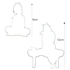May include: Two white silhouette cutouts of a seated figure, one 9 cm tall and the other 12 cm tall. The figures have a crown-like detail on their heads. The larger figure is seated at a table.