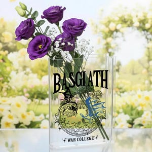 May include: A clear rectangular vase with the text "BASGIATH" and "WAR COLLEGE" printed on it. The vase holds purple flowers and white baby's breath. The background is a blurred image of a garden.