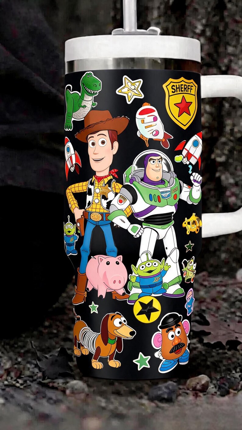 May include: A black stainless steel tumbler featuring a wrap-around graphic print of various animated characters including a cowboy, a space ranger, a green dinosaur, a pink pig, a dachshund, and a potato figure, with a white lid and handle.