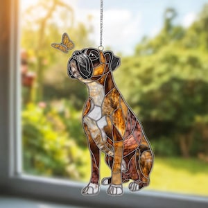 Puede incluir: Adorno de ventana de vidriera con un perro bóxer y una mariposa. El perro es marrón, blanco y negro, con un diseño de mosaico. La mariposa es amarilla y naranja. El adorno cuelga de una cadena plateada.
