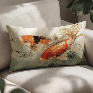 May include: Rectangular decorative pillow featuring two koi fish in shades of orange, white, and black. The fish are depicted in a watercolor style against a backdrop of muted greens and blues. The pillow is placed on a neutral-toned sofa.