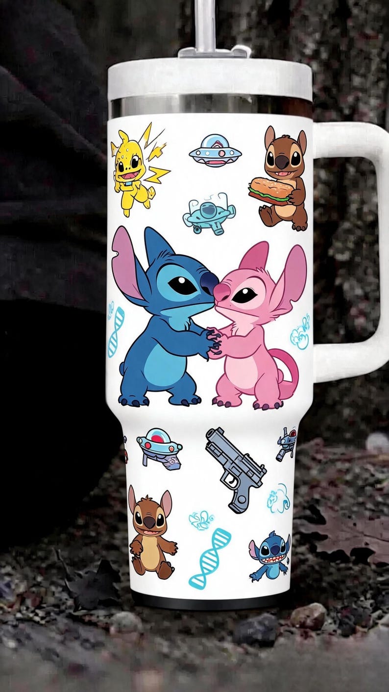 May include: A white stainless steel tumbler with a handle and lid, featuring a repeating pattern of blue and pink alien characters, a yellow creature, a grey handgun, blue DNA strands, small spaceships, and various small blue graphic icons.