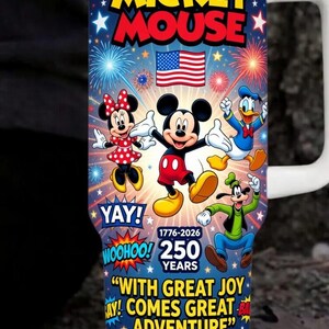 May include: A white-handled tumbler featuring Mickey Mouse and friends against a blue background with fireworks and stars. The tumbler celebrates 250 years with the text "Mickey Mouse", "Yay!", "Woohoo!", and "With great joy comes great adventure."
