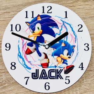May include: Round white wall clock featuring Sonic the Hedgehog in blue, red, and yellow. The clock face has black numerals and hands, with the name "JACK" printed below the character.