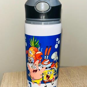 May include: A white water bottle with a grey lid and a blue graphic panel featuring Spongebob Squarepants characters including Patrick Star, Mr. Krabs, and Squidward. The name Jenson is printed in blue letters at the bottom of the graphic panel.