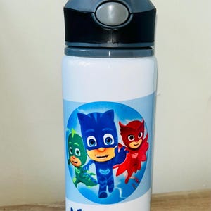 Könnte beinhalten: Eine weiße Wasserflasche mit einem blau-weißen Design mit Zeichentrickfiguren. Die Flasche hat einen grauen Deckel und Griff. Der Name "LEANDRO" ist blau auf der Unterseite der Flasche aufgedruckt.