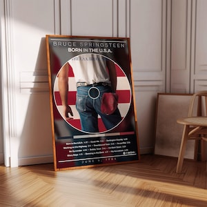 May include: Framed poster featuring Bruce Springsteen's "Born in the U.S.A." album cover. The image shows a man's back with a red cap in his pocket, set against a backdrop of the American flag. The poster includes the album's tracklist and the date June 4, 1984.