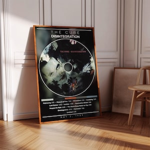 Könnte beinhalten: Gerahmtes Poster für das Album "Disintegration" von The Cure. Das Albumcover zeigt ein kreisförmiges Bild mit einem Gesicht und floralen Elementen. Das Poster enthält den Albumtitel, den Bandnamen, die Titelliste und das Datum 2. Mai 1989.