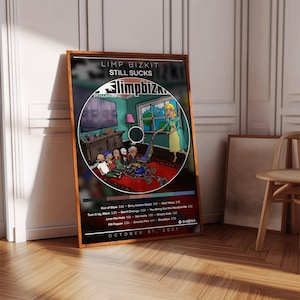 May include: A framed poster featuring the album art for Limp Bizkit's "Still Sucks." The artwork depicts a cartoon scene inside a CD, with the album title and tracklist visible. The frame is brown.