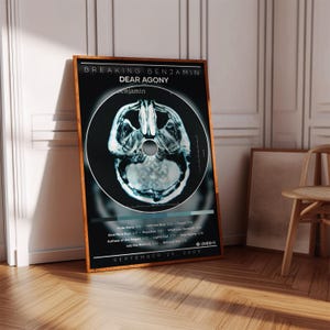 May include: A rectangular poster featuring the Breaking Benjamin Dear Agony album cover with a black background, a central brain scan image, white text listing track titles and durations, and the release date September 29, 2009, in a wooden frame.